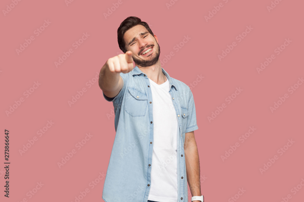 Portrait of funny happy handsome bearded young man in blue casual style shirt standing pointing and looking at camera with toothy smile. indoor studio shot, isolated on pink background. Portrait of funny happy handsome bearded young man in blue casual style shirt standing pointing and looking at camera with toothy smile. indoor studio shot, isolated on pink background.