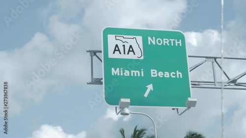 Road Signage on American highway going to North Miami Beach. Cloudy blue sky the day. Slow motion. RoadSign. Palm trees. Cars and skyscrapers. Close up.