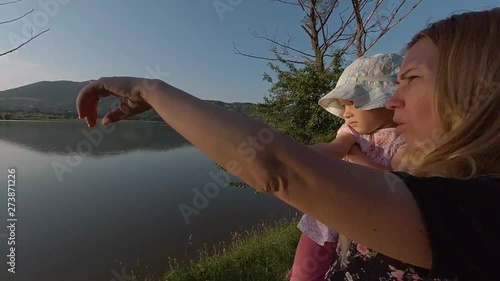 Slow motion of mother and little girl. Fammily sunset moment on the shore of a lake. Mother shows something in the distance to her daughter photo