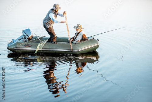 Grandfather with adult son fishing on the inflatable boat on the lake early in the morning