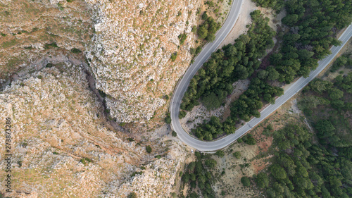  Aerial view of mountain curve road. Green forest at sunset in summer in Europe. Landscape with asphalt road, car, trees on the rocks. Roadway through the park. 