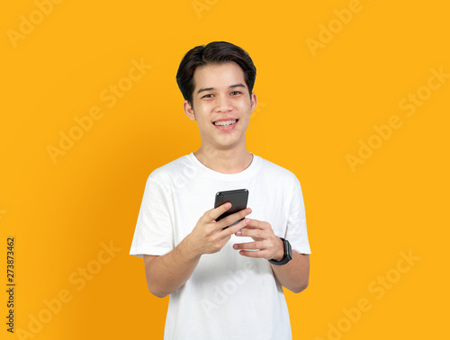 Young smiling Asian man with holding smart phone on orange background. copy space for put advertisement. © sitthiphong