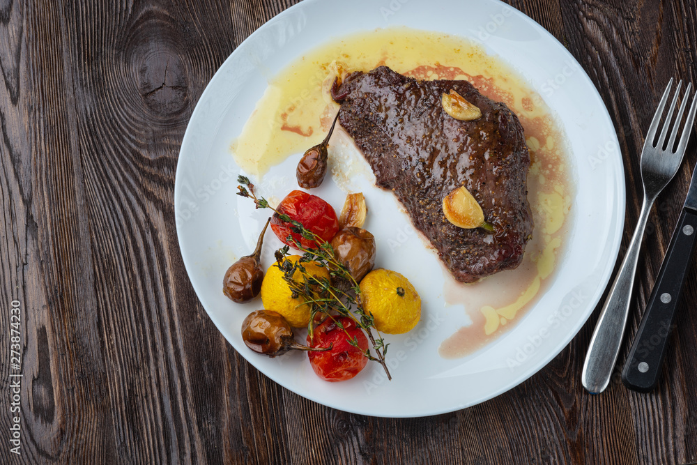 Rib-eye steak with baked vegetables resting on a white plate Rib-eye steak with baked vegetables resting on a white plate