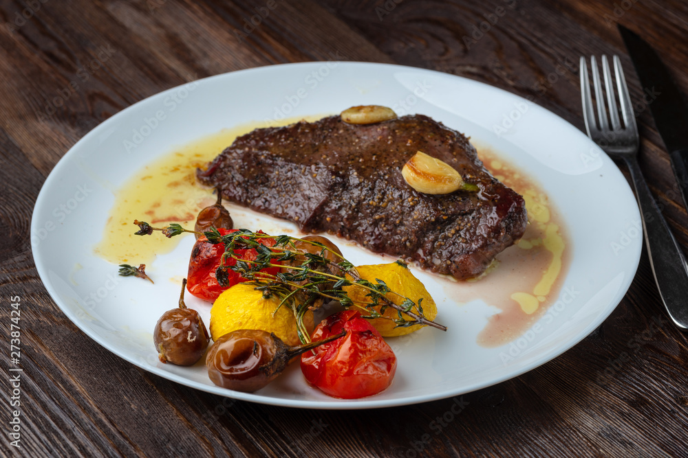 Rib-eye steak with baked vegetables resting on a white plate Rib-eye steak with baked vegetables resting on a white plate