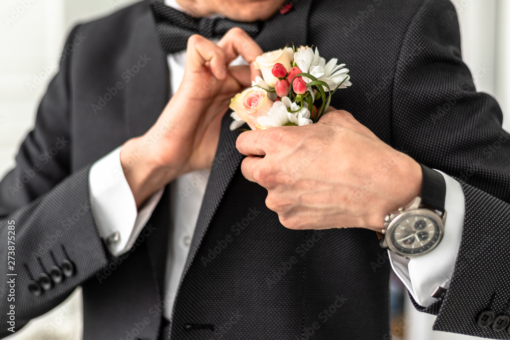 The groom in a white shirt, tie, black or dark gray and costume. Young man with a beautiful boutonniere of pink roses or chrysanthemums and green leaves, on the lapel of his jacket. Wedding theme The groom in a white shirt, tie, black or dark gray and costume. Young man with a beautiful boutonniere of pink roses or chrysanthemums and green leaves, on the lapel of his jacket. Wedding theme