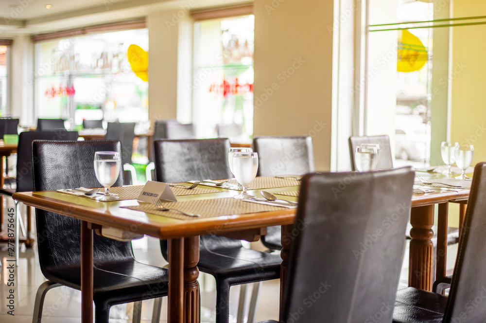 The tables and chairs in the restaurant with full set preparation next to the window with flare in the afternoon. 