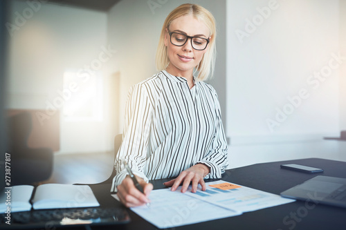 Smiling businesswoman signing a document while working in an off
