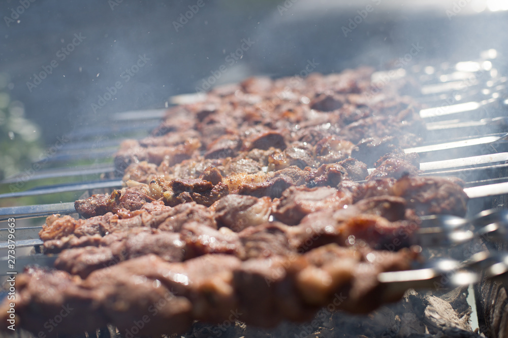 Naklejka Shashlik or shashlyk preparing on a barbecue grill over charcoal. Grilled cubes of pork meat on metal skewer. Meat on skewers is roasted on fire