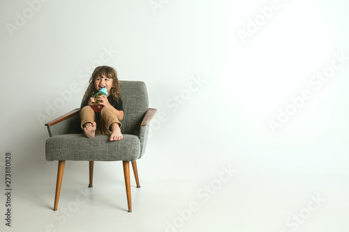 Little child sitting and playing in armchair isolated on white studio background. Young boy with blonde hair looks interested of world surrounded him. Concept of childhood, happiness, emotions. © master1305