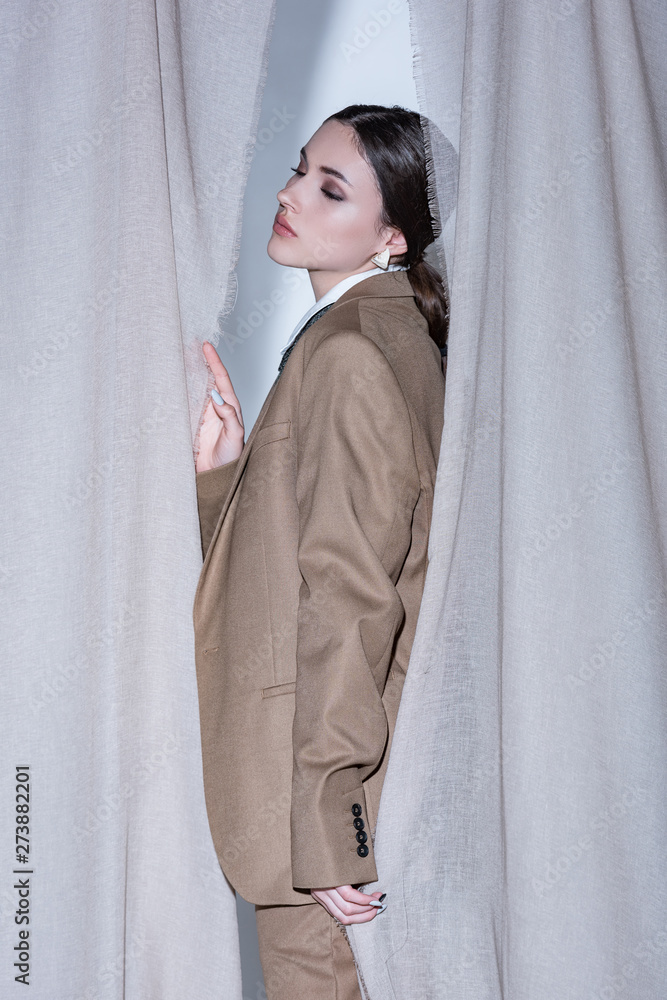side view of fashionable woman in suit standing on light grey curtain background side view of fashionable woman in suit standing on light grey curtain background