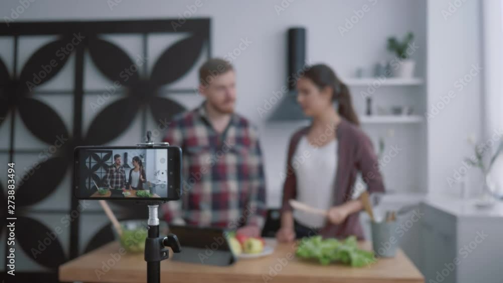 nutritional blog, young vloggers man and woman prepare healthy breakfast with vegetables and greens in kitchen while camera smartphone records video for subscribers at social networks nutritional blog, young vloggers man and woman prepare healthy breakfast with vegetables and greens in kitchen while camera smartphone records video for subscribers at social networks