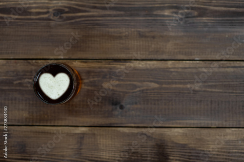 Mug of beer with silhouettes of a heart on dark wooden background. Empty space for text
