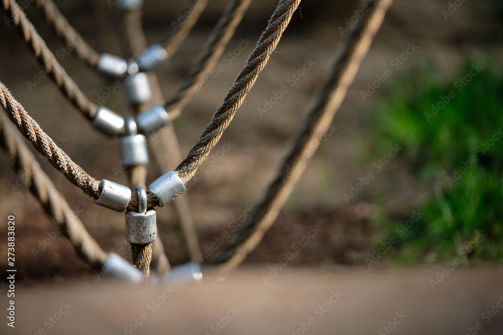 Abstract picture shot on a playground at a climbing frame with a detail with beige ropes connected via metal.