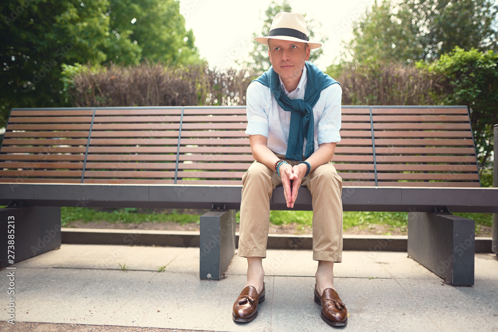 Fototapeta premium Full length portrait of a guy sitting on a bench in a hat 