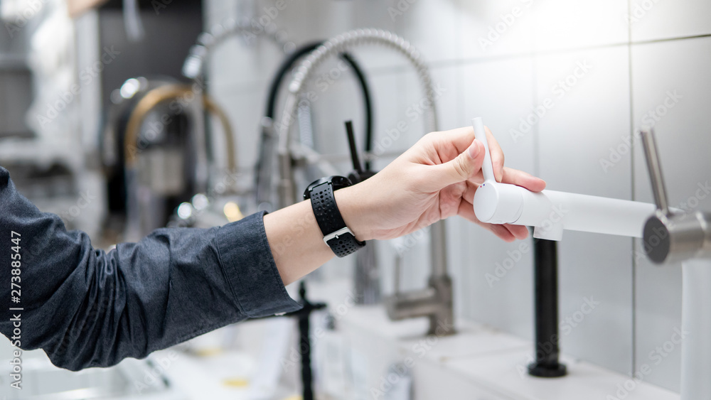 Male hand choosing modern white water tap in furniture store. Home improvement for domestic kitchen. Male hand choosing modern white water tap in furniture store. Home improvement for domestic kitchen.