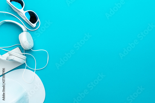 Flat lay image of modern teenager accessories background - headphones, sunglasses, smartphone, baseball cap. Top view of white accessories on turquoise blue background with copy space
