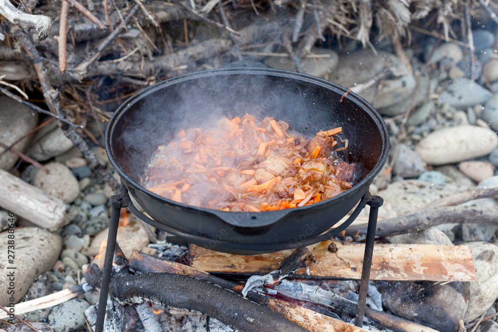 Meat and vegetables are fried in a pilaf cauldron over a fire. Cooking food in nature. National cuisine. Horizontal photo of food. Meat and vegetables are fried in a pilaf cauldron over a fire. Cooking food in nature. National cuisine. Horizontal photo of food.
