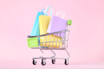 Small metal cart with shopping bags on pink background
