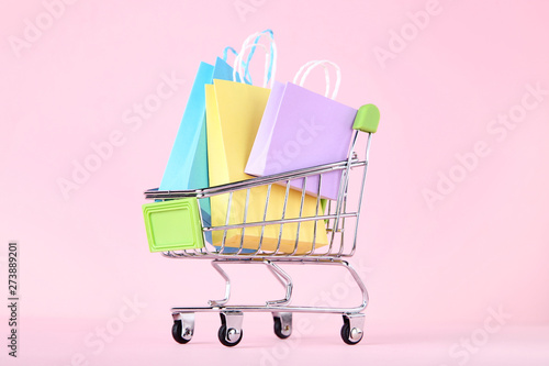 Small metal cart with shopping bags on pink background