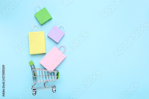 Small metal cart with shopping bags on blue background