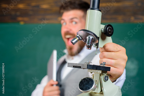 College teacher with computer and microscope. Research. Excited tutor in classroom. Happy scientist with laptop and microscope. Bearded man with notebook and microscope. Selective focus on microscope.