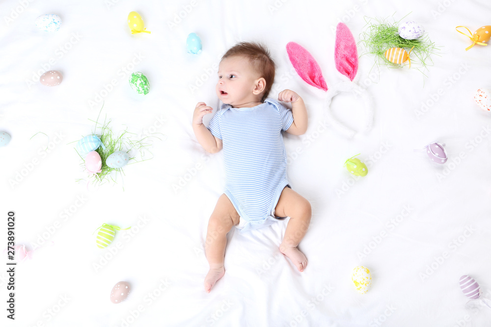 Cute baby with easter eggs and rabbit ears lying on white bed Cute baby with easter eggs and rabbit ears lying on white bed