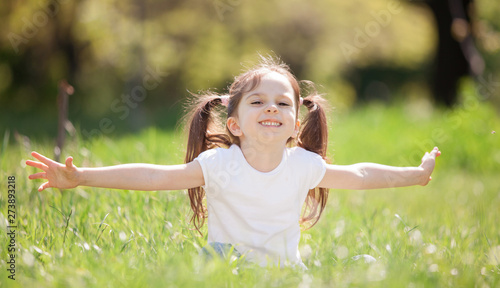 Fun little girl play in the park. Beauty nature scene with colorful background at summer or spring season. Family outdoor lifestyle. Happy girl relax on green grass
