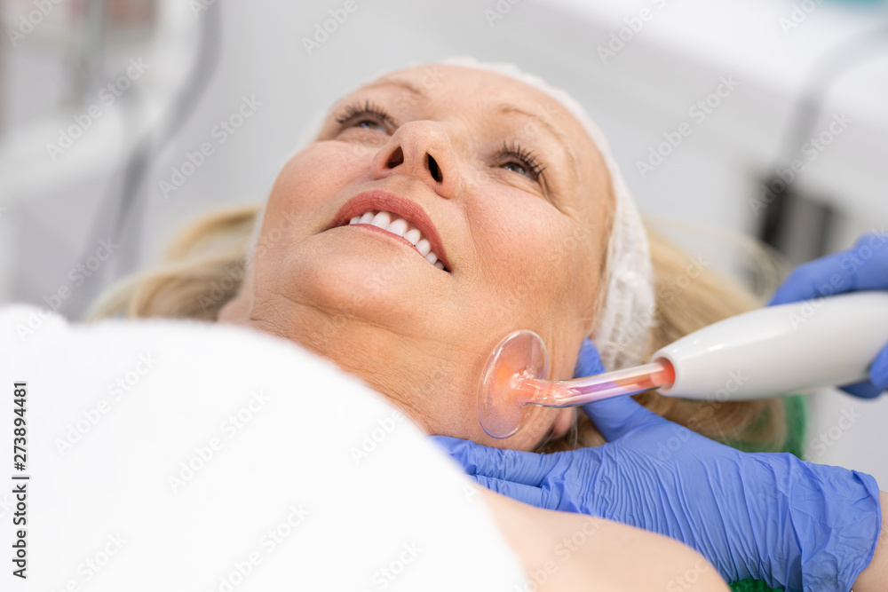 Receiving electric darsonval facial massage procedure at beauty salon Receiving electric darsonval facial massage procedure at beauty salon