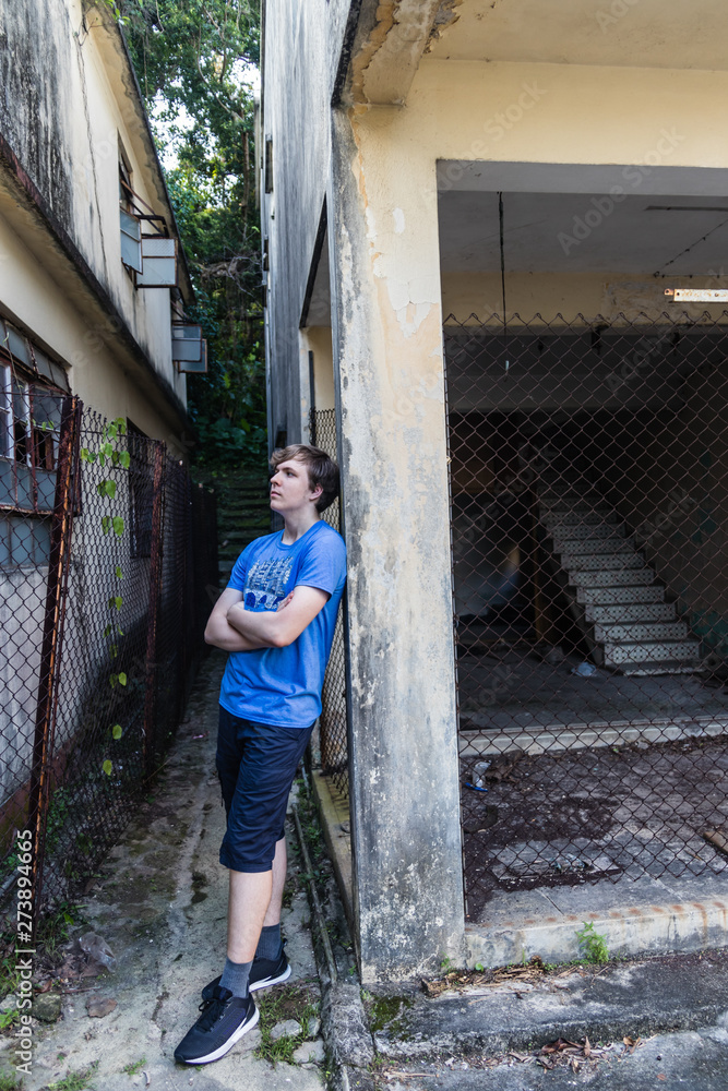 A handsome teenager with crossed arms and leaning on the wall in the abandoned village A handsome teenager with crossed arms and leaning on the wall in the abandoned village
