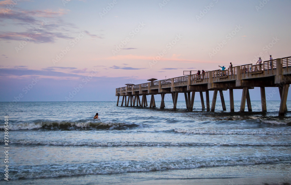 People surfing by pier in the sunset