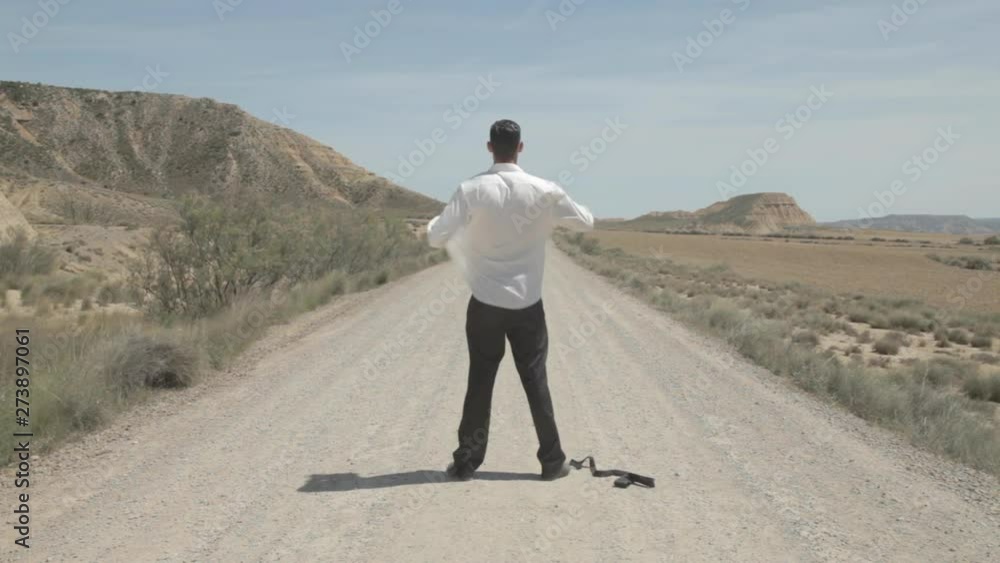 Handsome caucasian businessman in white shirt, feeling freedom, standing and alone and removing his shirt and black tie in the desert and start running to the mountain in sunny summer with a big sun. Handsome caucasian businessman in white shirt, feeling freedom, standing and alone and removing his shirt and black tie in the desert and start running to the mountain in sunny summer with a big sun.