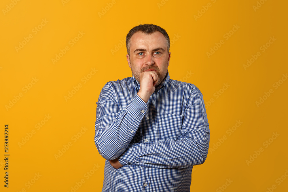 Pensive man holding hand on chin and looking at camera. Yellow background. Closeup portrait. Pensive man holding hand on chin and looking at camera. Yellow background. Closeup portrait.