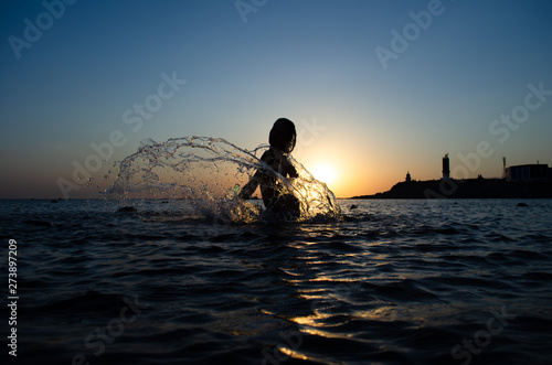 Silhouette of young girl in the water that splashing their hair against sunset