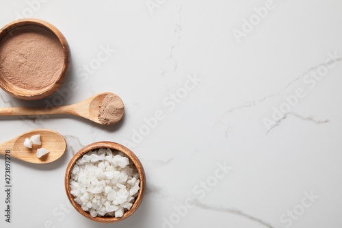 top view of clay powder and sea salt in wooden bowls and spoons on marble table
