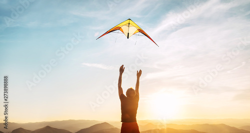 Foto Man starting to fly bright kite in sunset sky over the high mountain