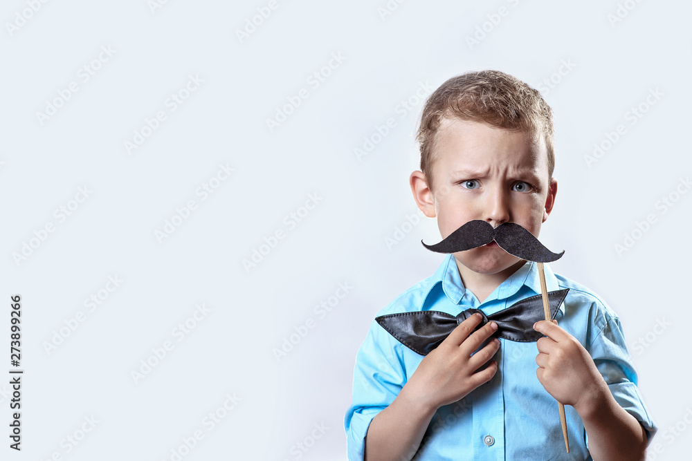 frowning serious boy in a light shirt put a mustache on a stick and a bow tie on his face to make him look older.