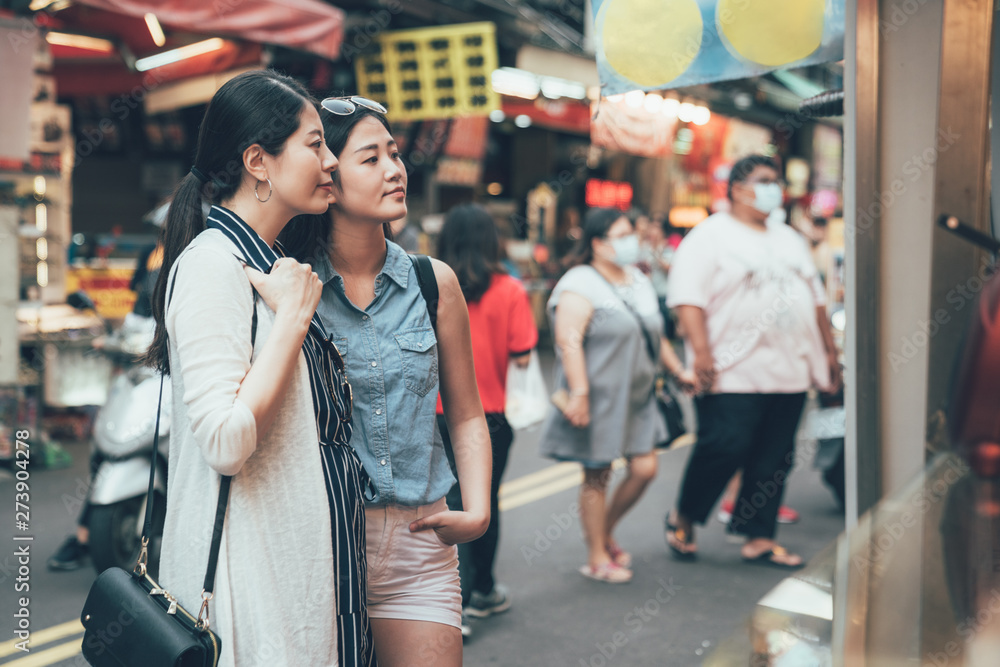 Happy women tourists standing on road street looking at food vendor cart outdoors in local market. two young girls travelers together waiting for order meal. trip in japan downtown lifestyle taiwan