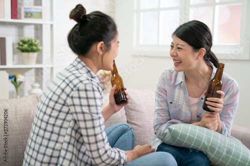 Two best friends. Young asian women having conversation sitting on couch holding beer bottle. beautiful girls sisters enjoy drink alcohol on sofa laughing cheerful relax in home living room day time