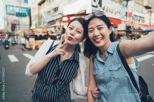 Friends having fun outdoors. two asian girls travelers with sunglasses standing on street by zebra cross making self portrait. cute women tourists taking selfie on city urban road taiwan taipei photo