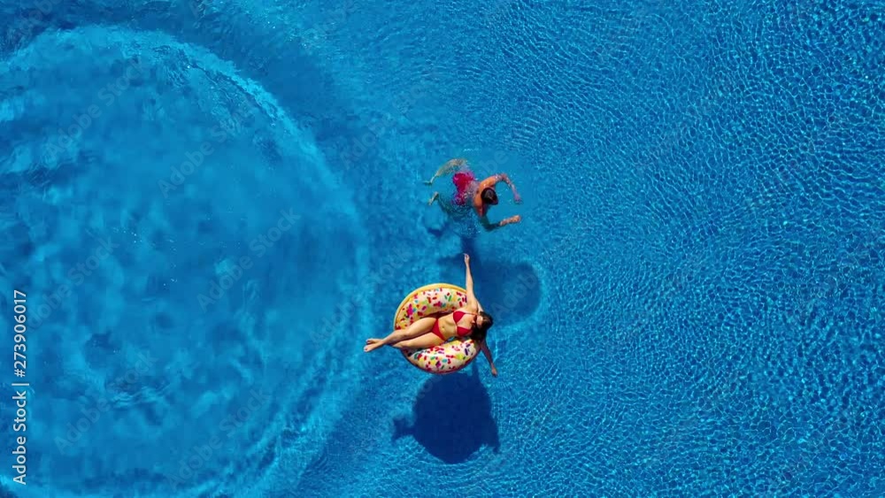 Aerial view of man dives into the the pool while girl is lying on a donut pool float
