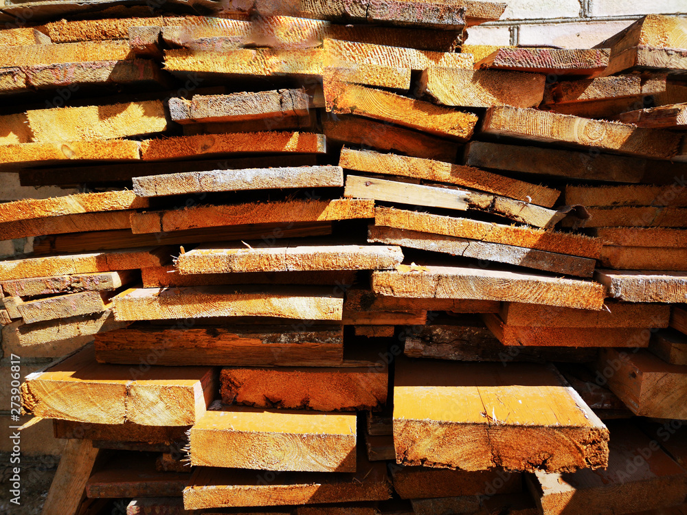 Wood wooden yellow and brown boards close-up lie in the section, stacked in a row, on each other floors, summer Sunny day. The texture of wood boards. Wood wooden yellow and brown boards close-up lie in the section, stacked in a row, on each other floors, summer Sunny day. The texture of wood boards.