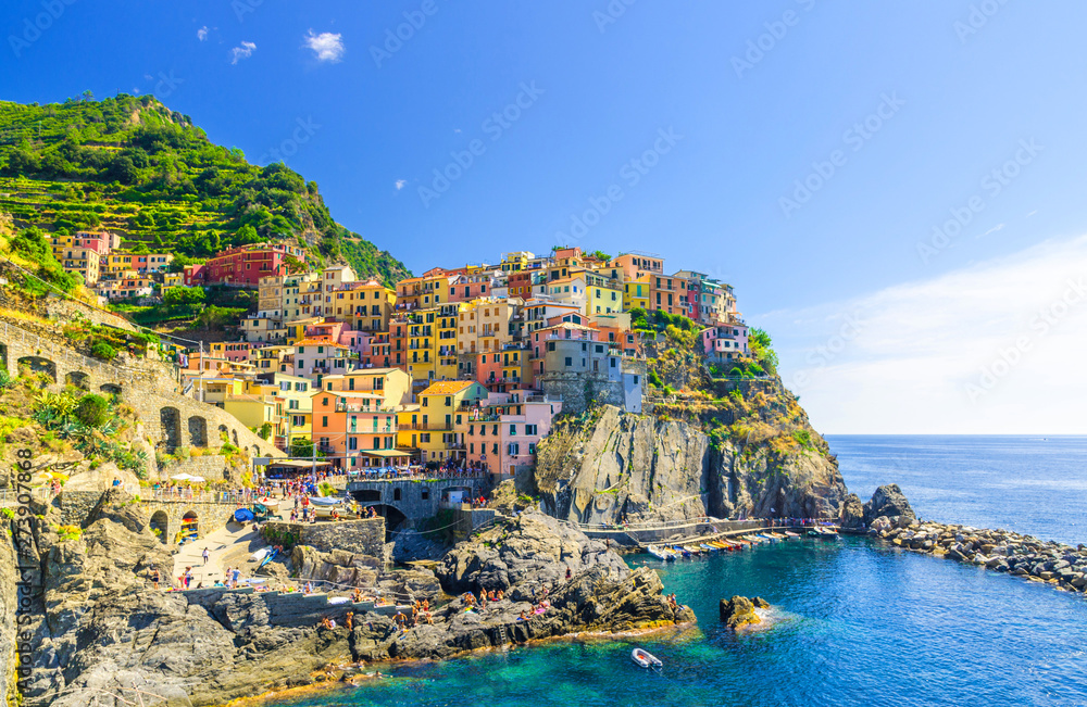 Manarola traditional typical Italian village in National park Cinque Terre with colorful multicolored buildings houses on rock cliff and marine harbor, blue sky background, La Spezia, Liguria, Italy