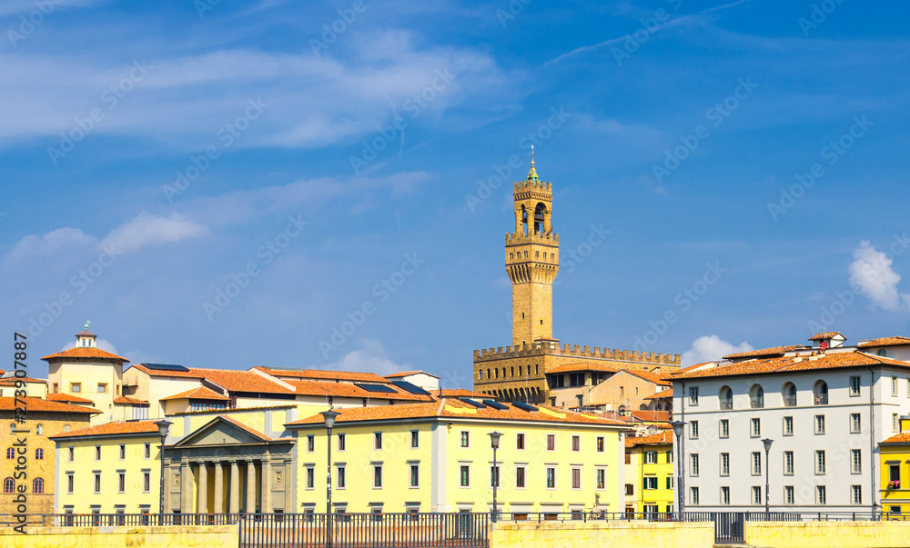Bell tower of Palazzo Vecchio palace and buildings on embankment promenade in historical centre of Florence city with blue sky background, Tuscany, Italy