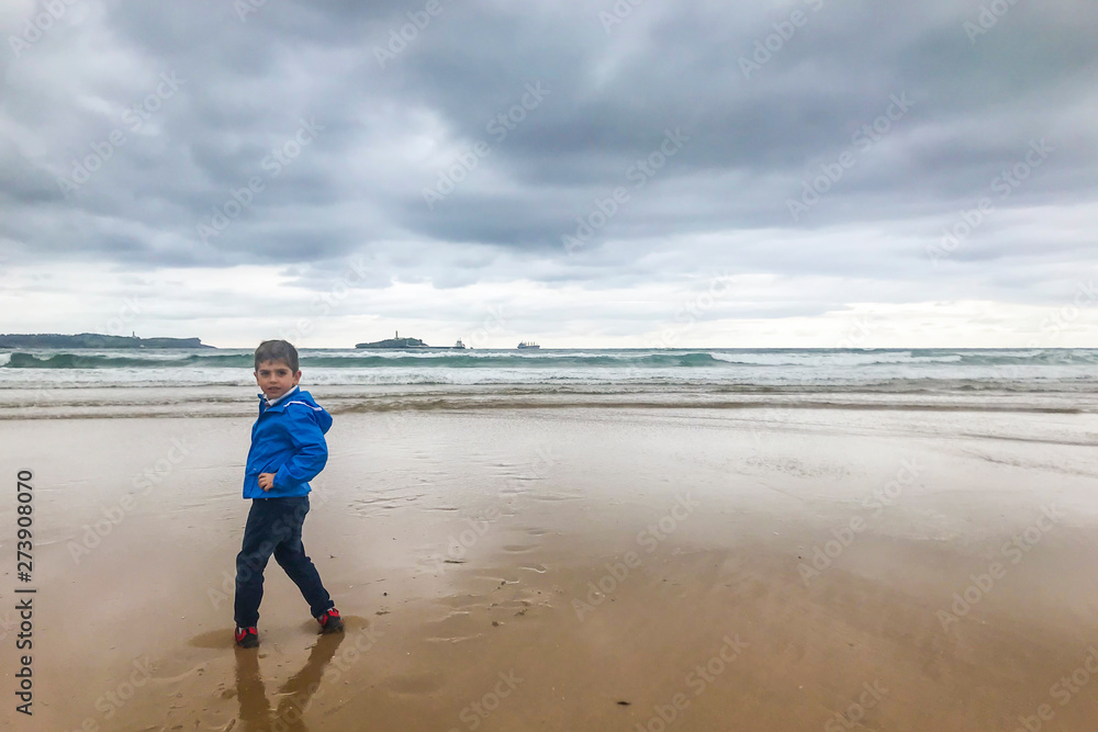Little kid on the beach in a day with a stormy clous