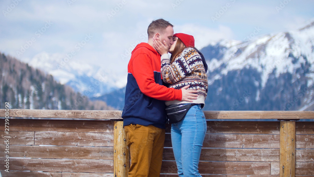 A young couple tourists standing on a background of mountains and kiss A young couple tourists standing on a background of mountains and kiss