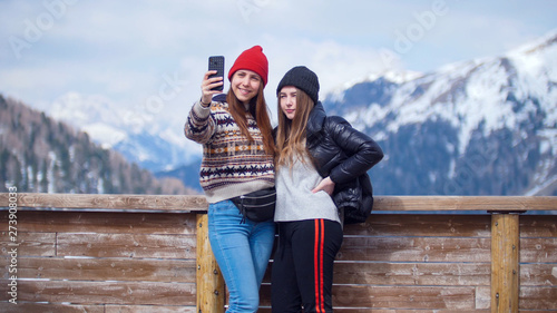 Two young women tourist standing on a background of mountains and taking a selfie on the phone