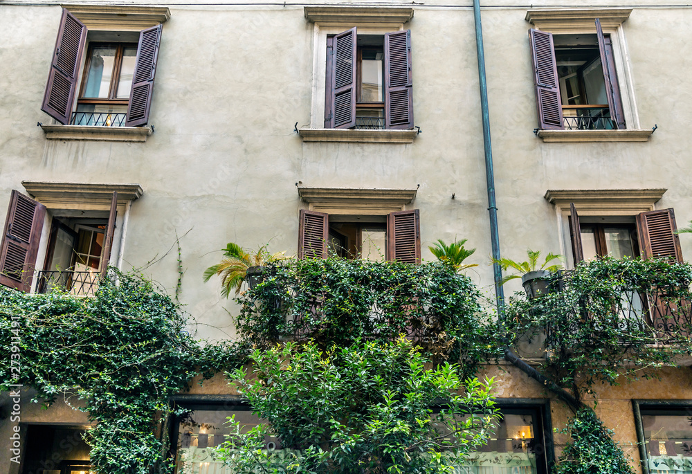 Facade of an Italian house with wooden shutters on the windows and plants on the balconies
