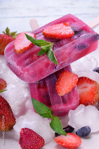 Berry popsicles with pieces of strawberry and honeysuckle on the white plate