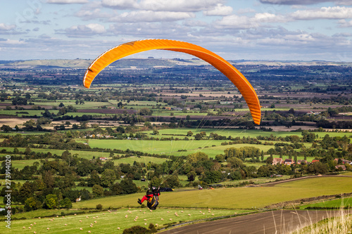 Paraglider with yellow parachute gliding over green landscape