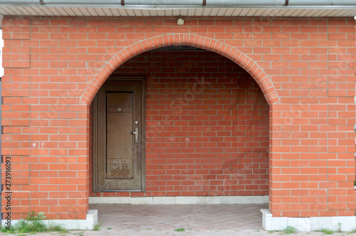 Old village country house with an inviting entrance on cobblestone through a brown door set in a red arch brick wall